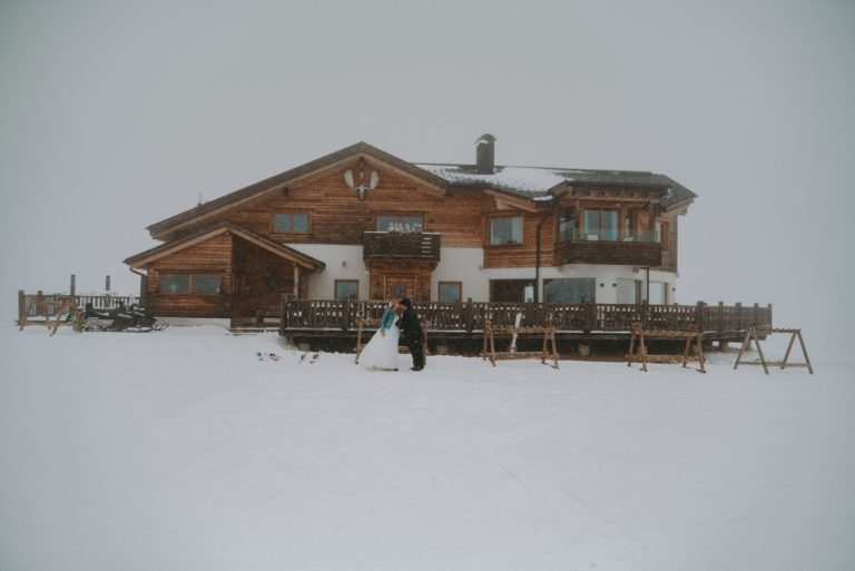 bride and groom kissing in a snowstorm in front of a mountain hut Cherz in the Dolomites