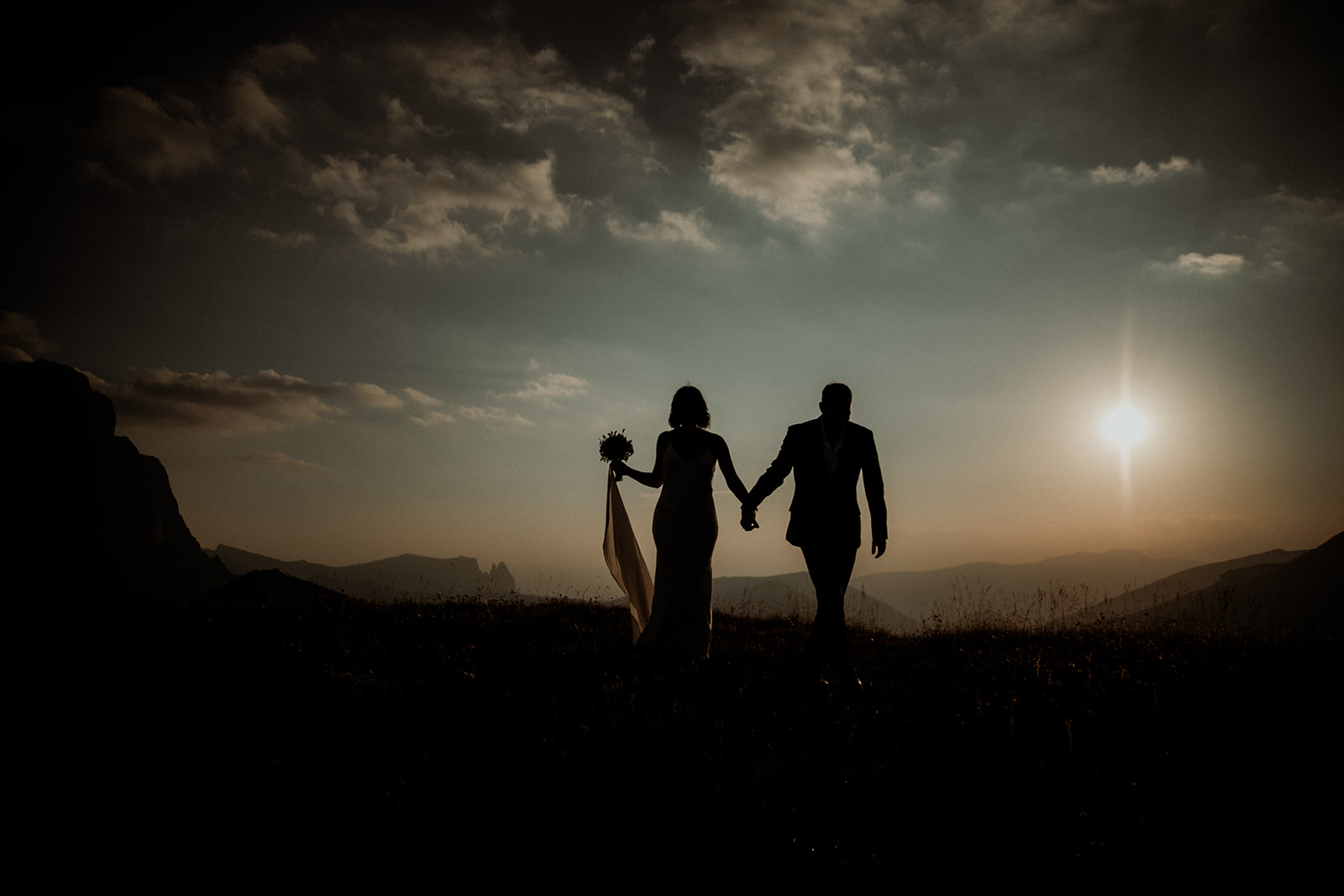 Dolomites Elopement - Couple silhouette holding hands at sunset in the mountains.