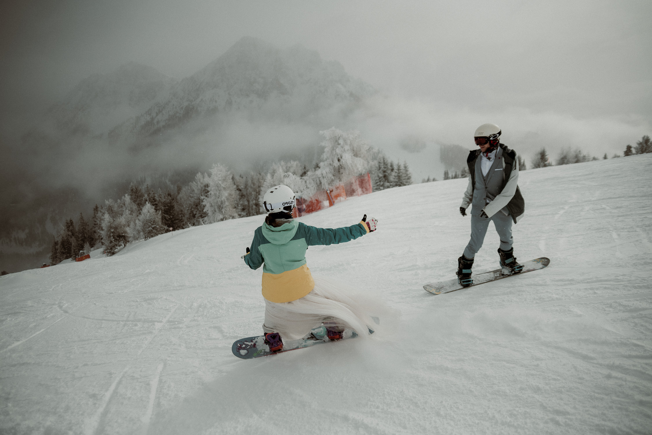 Winterhochzeit auf dem Snowboard - Pärchen fährt snowboard mit Hochzeitskleidung